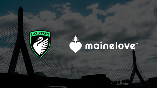 Boston Legacy FC crest and mainelove logo displayed over a Boston skyline featuring the Zakim Bridge, highlighting the club’s sustainability partnership