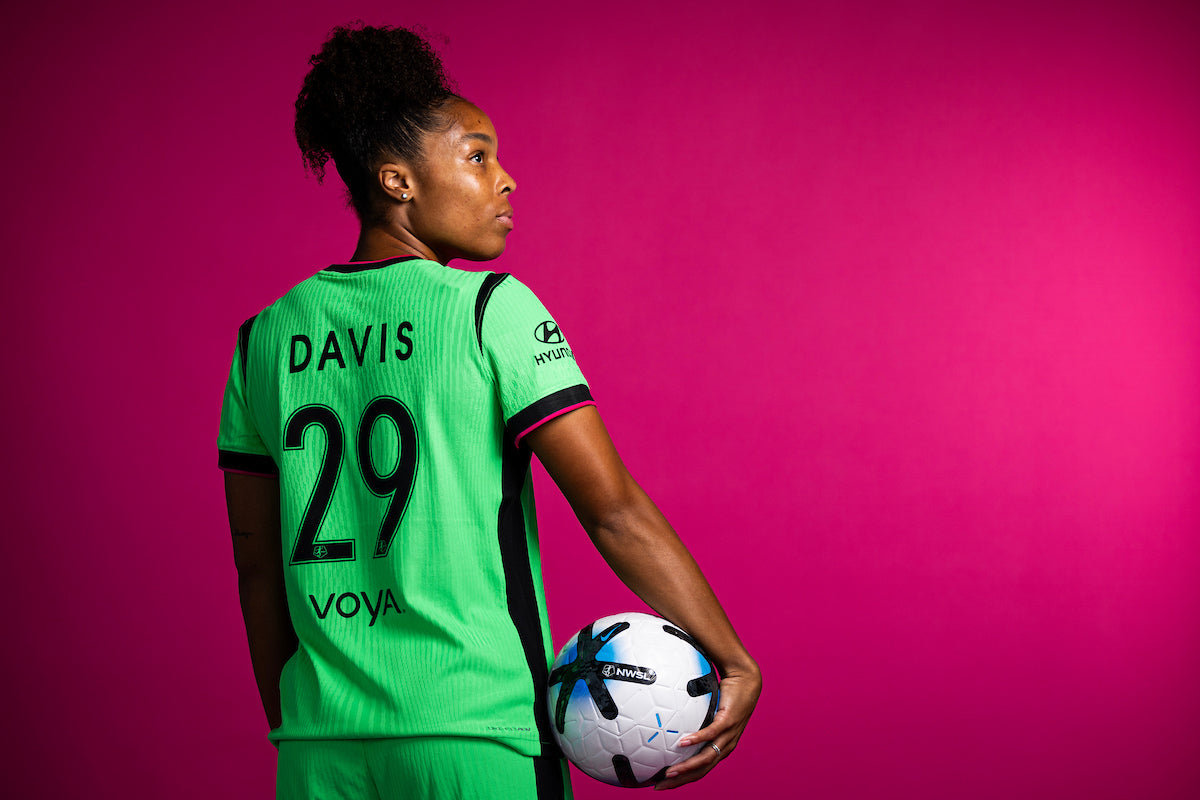 Boston Legacy FC player Davis, number 29, poses in a green NWSL kit against a magenta background, holding an official NWSL match ball while looking over her shoulder.